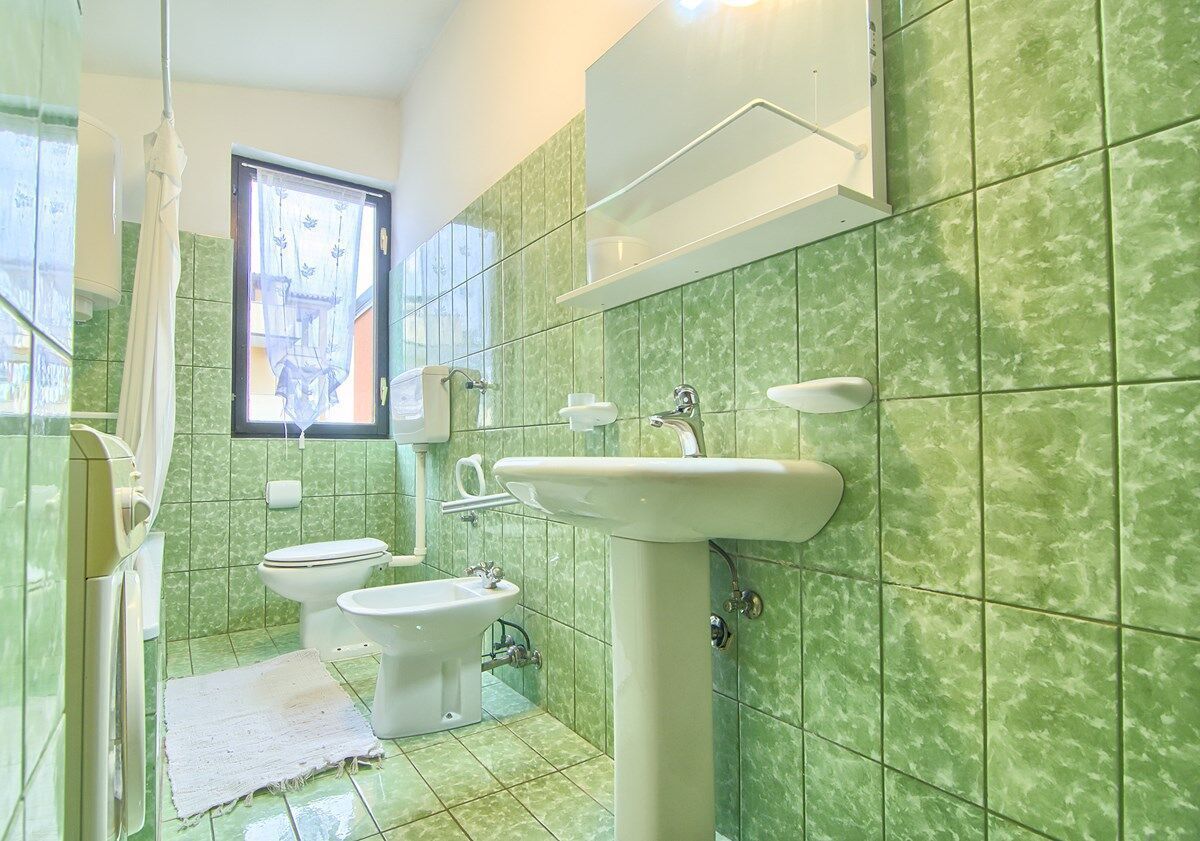 Ein Badezimmer mit grünen Fliesen, zwei Toiletten, einem Analfassgerät und einem Waschbecken.