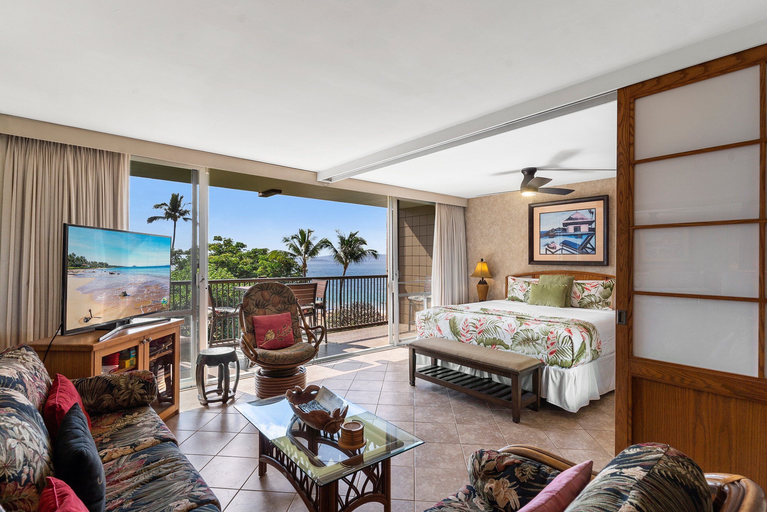 A spacious living area with a balcony, a television, a bed, and a dining table.
