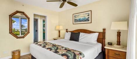 A hotel room with a bed, a ceiling fan, a nightstand with a lamp, a framed picture on the wall, and a door leading to a balcony.