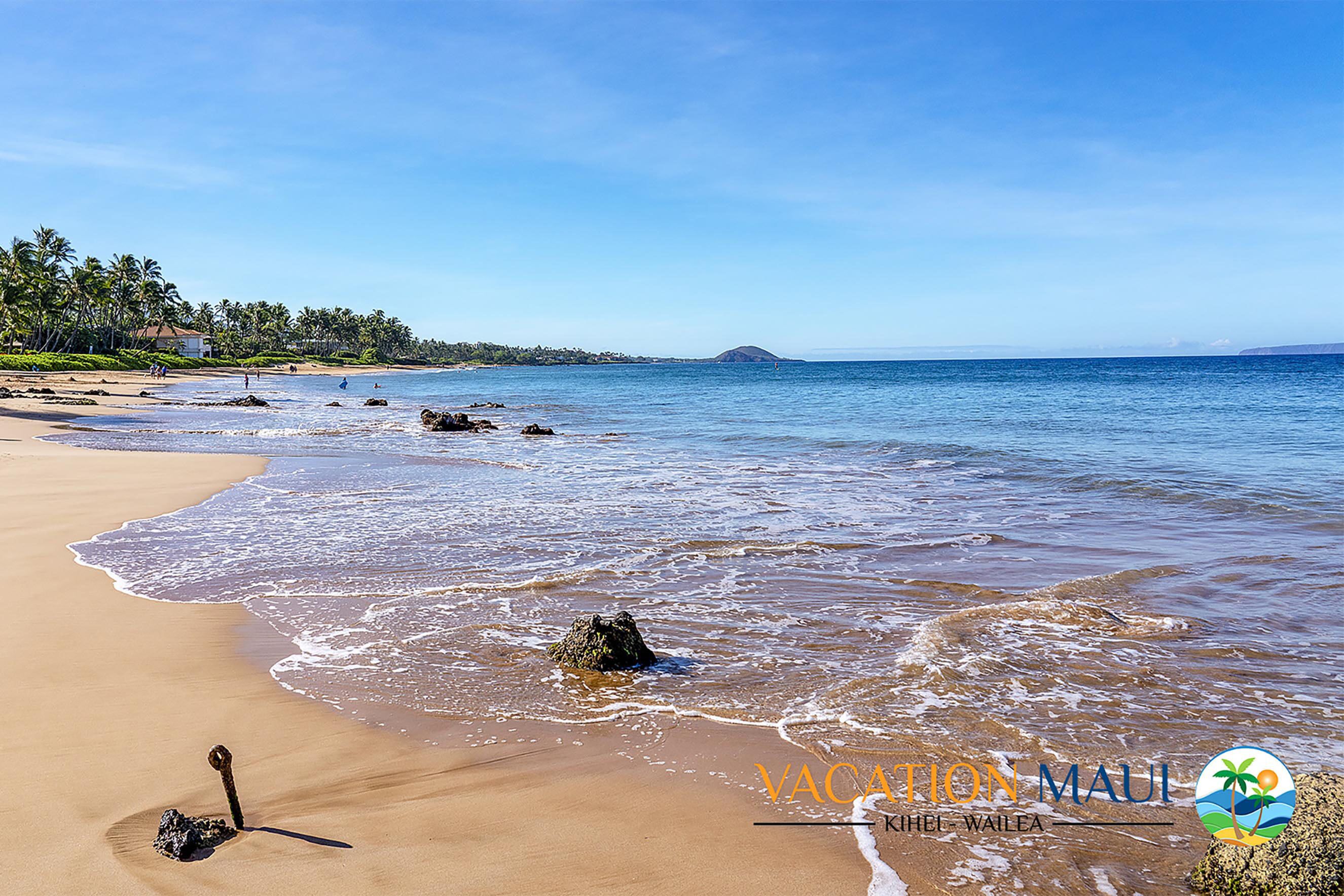 A beach with clear skies, calm waters, and a few people in the distance.
