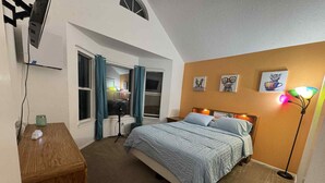 Un dormitorio con cama, escritorio, ventilador de pie y lámpara de pie.