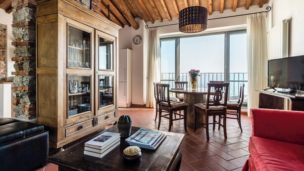 A spacious living area with a wooden cabinet, a dining table with chairs, a red sofa, and a television. - Panoramic Appatamento Borgo di Matraia (Matraia)