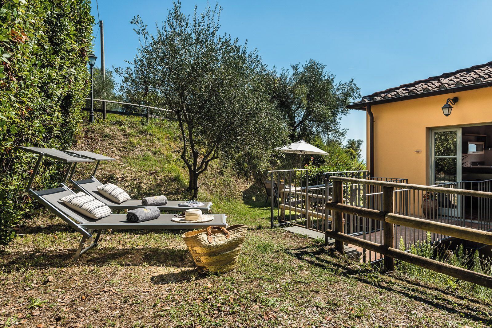A sunlit outdoor area with lounge chairs, a table with a basket, and a building with a balcony.