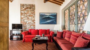 A living room with a red sofa, a television, a stone wall, and a large window with a geometric pattern. - Panoramic Appatamento Borgo di Matraia (Matraia)
