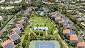 An aerial view of a residential area with solar panels on buildings, a tennis court, and a swimming pool. - Maui Hill (Kihei)