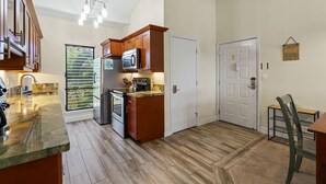 A kitchen with wooden cabinets, a microwave, and a stainless steel refrigerator. - Maui Hill (Kihei)