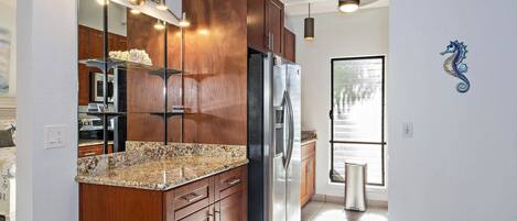 Una cocina moderna con armarios de madera, refrigerador de acero inoxidable, encimeras de granito y horno empotrado.