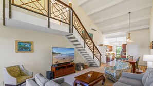 A spacious living room with a staircase, a television, and a kitchen in the background. - Maui Hill (Kihei)