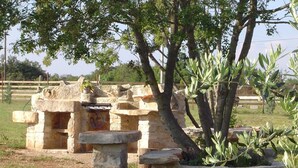 Una estructura de piedra con un banco y una mesita, rodeada de árboles y césped.