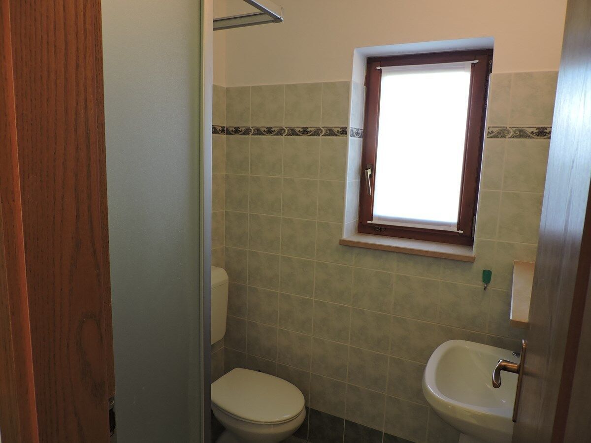 Un bagno piccolo con il water, un lavandino e una finestra sopra al lavandino.