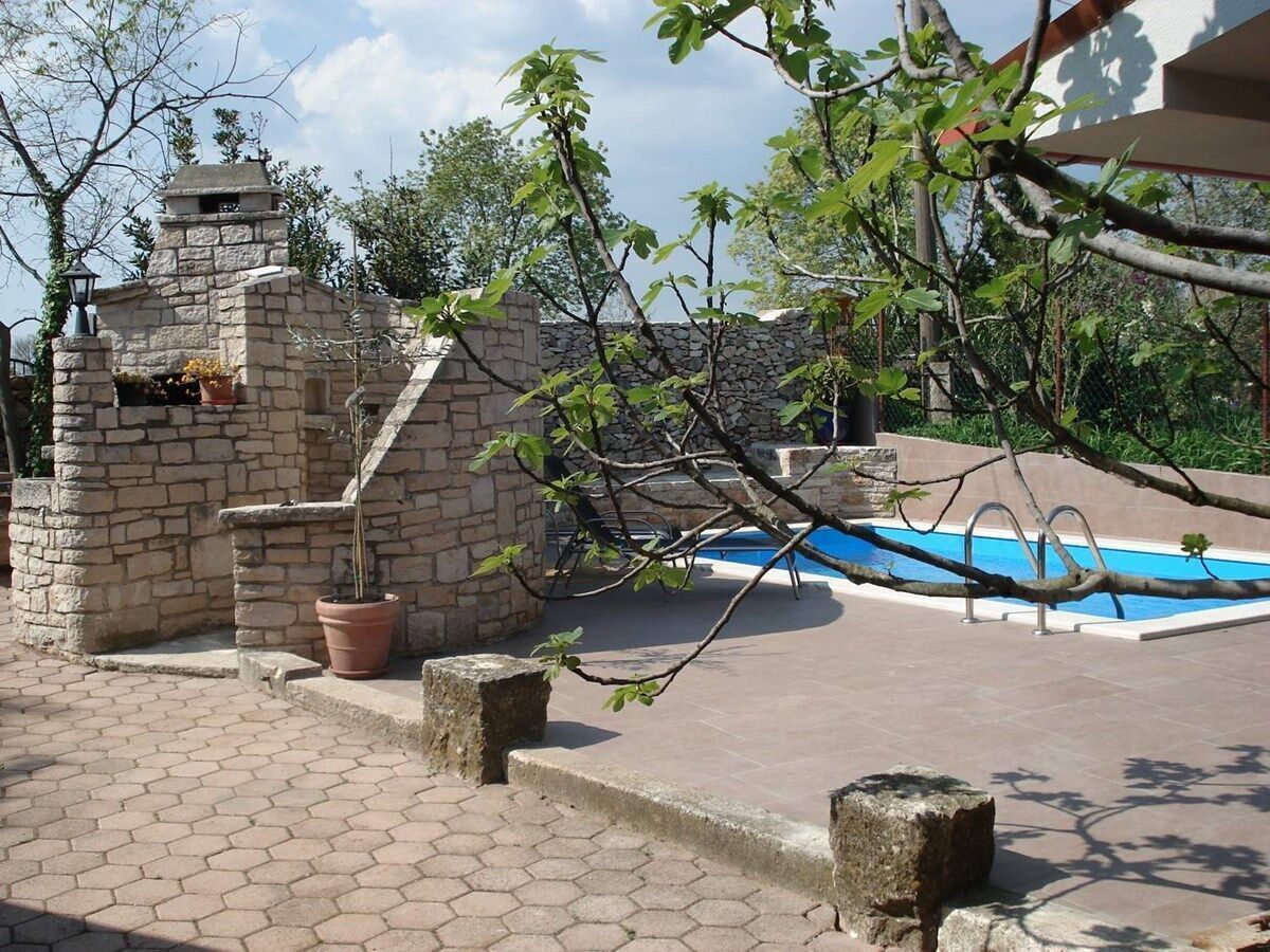 Ein Gebäude aus Stein mit einem Pool, umgeben von Kübelpflanzen und Bäumen.