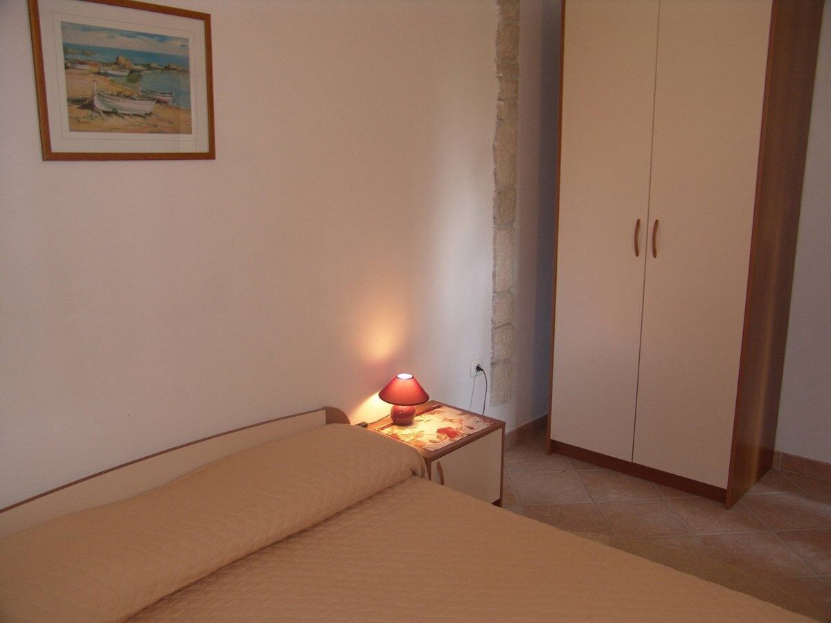 Ein kleines Schlafzimmer mit einem Einzelbett, einem Nachttisch mit Lampe, einem Kleiderschrank und einem Bild an der Wand.