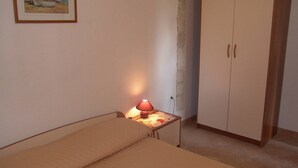 Un dormitorio pequeño con una cama individual, una mesita de noche con lámpara, un armario y un cuadro en la pared.