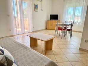 Ein Wohnzimmer mit einer Couch, einem Holztisch, einem Fernseher und einem Essbereich mit Stühlen.