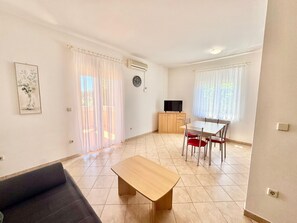 A living room with a sofa, a wooden table, a TV, and a dining area with chairs. - Apartments Cukon (16136-A3) - Medulin (Medulin)