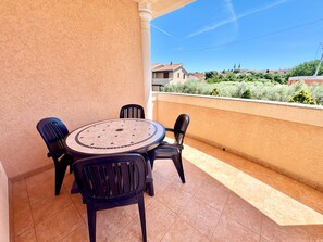 Ein Balkon mit rundem Tisch, vier Stühlen, gefliestem Boden und Blick auf Gebäude und Grünflächen.