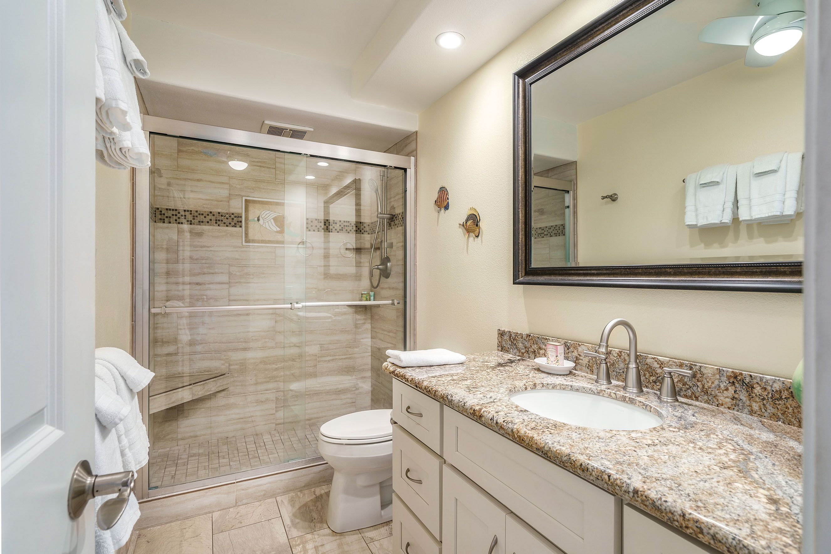 A modern bathroom with a glass-enclosed shower, a white toilet, a sink with a marble countertop, and a large mirror.