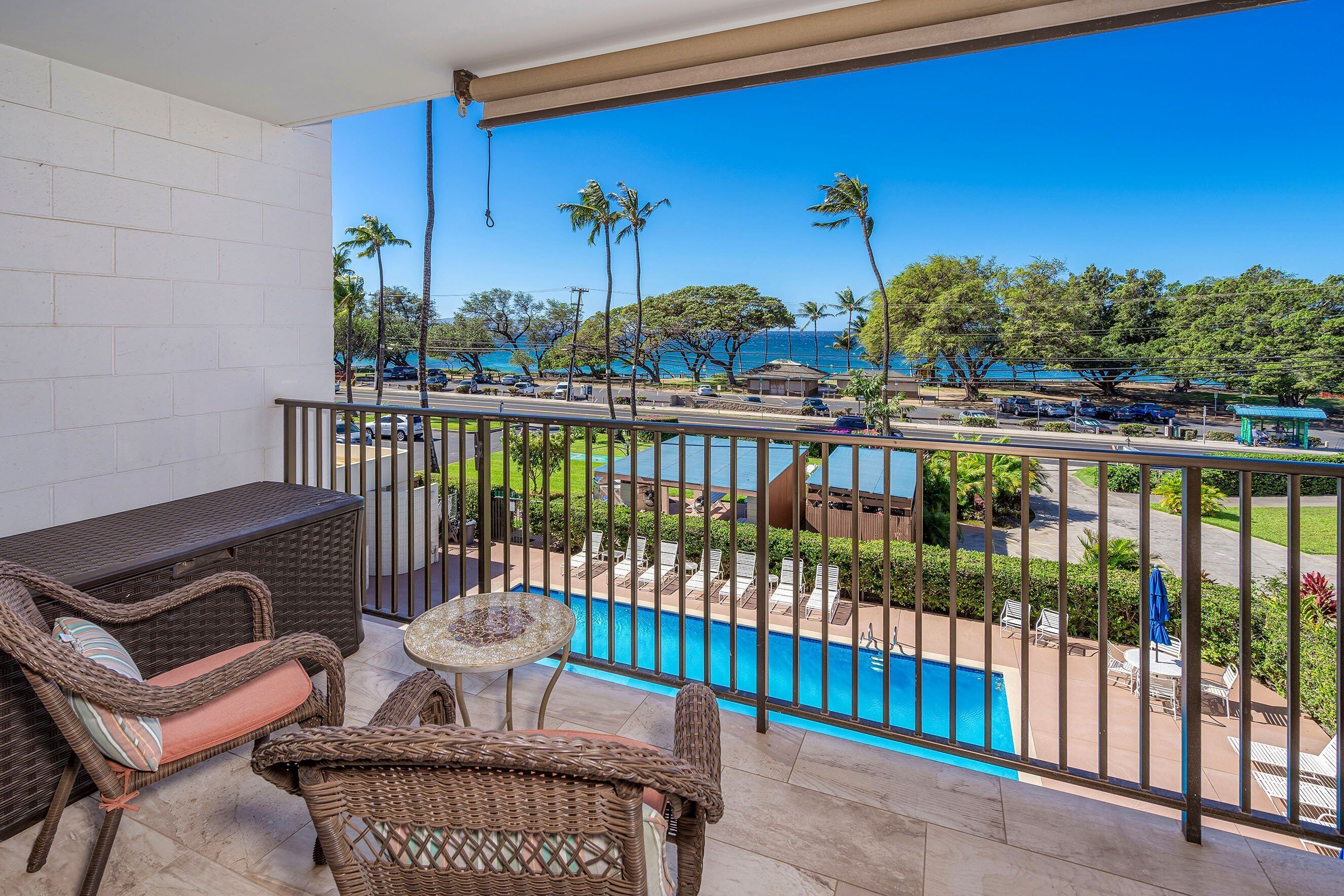 A balcony with wicker furniture, a view of a swimming pool, and a clear blue sky.