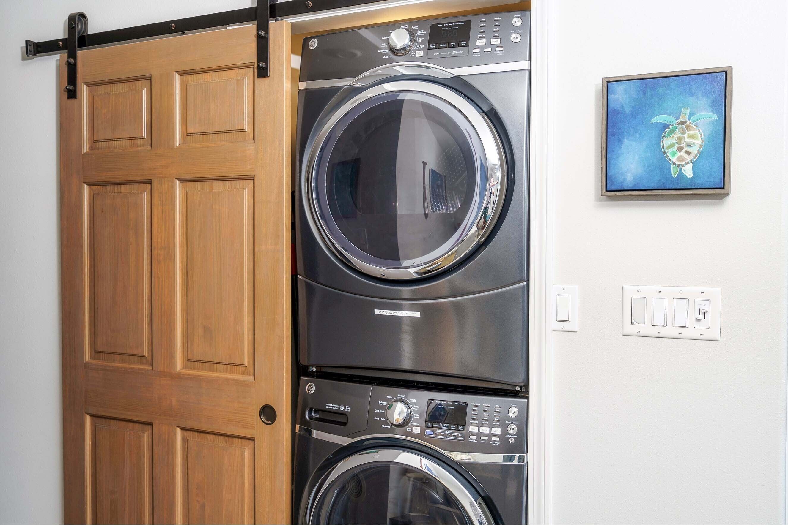 A stacked washer and dryer unit with a wooden sliding door and a framed artwork on the wall.