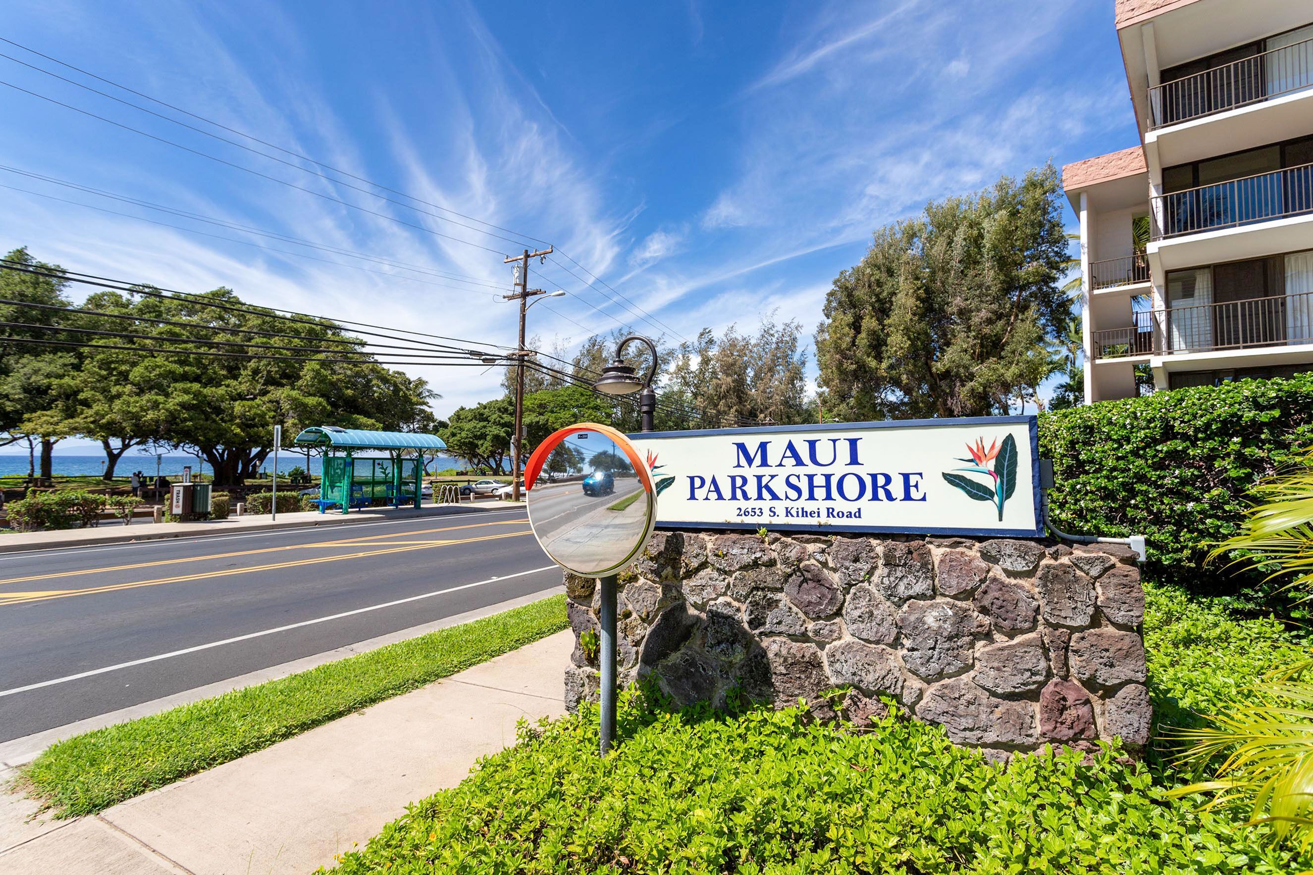 Segnale stradale per Maui Parkshore, con strada ben visibile, una fermata dell'autobus e un edificio sullo sfondo.