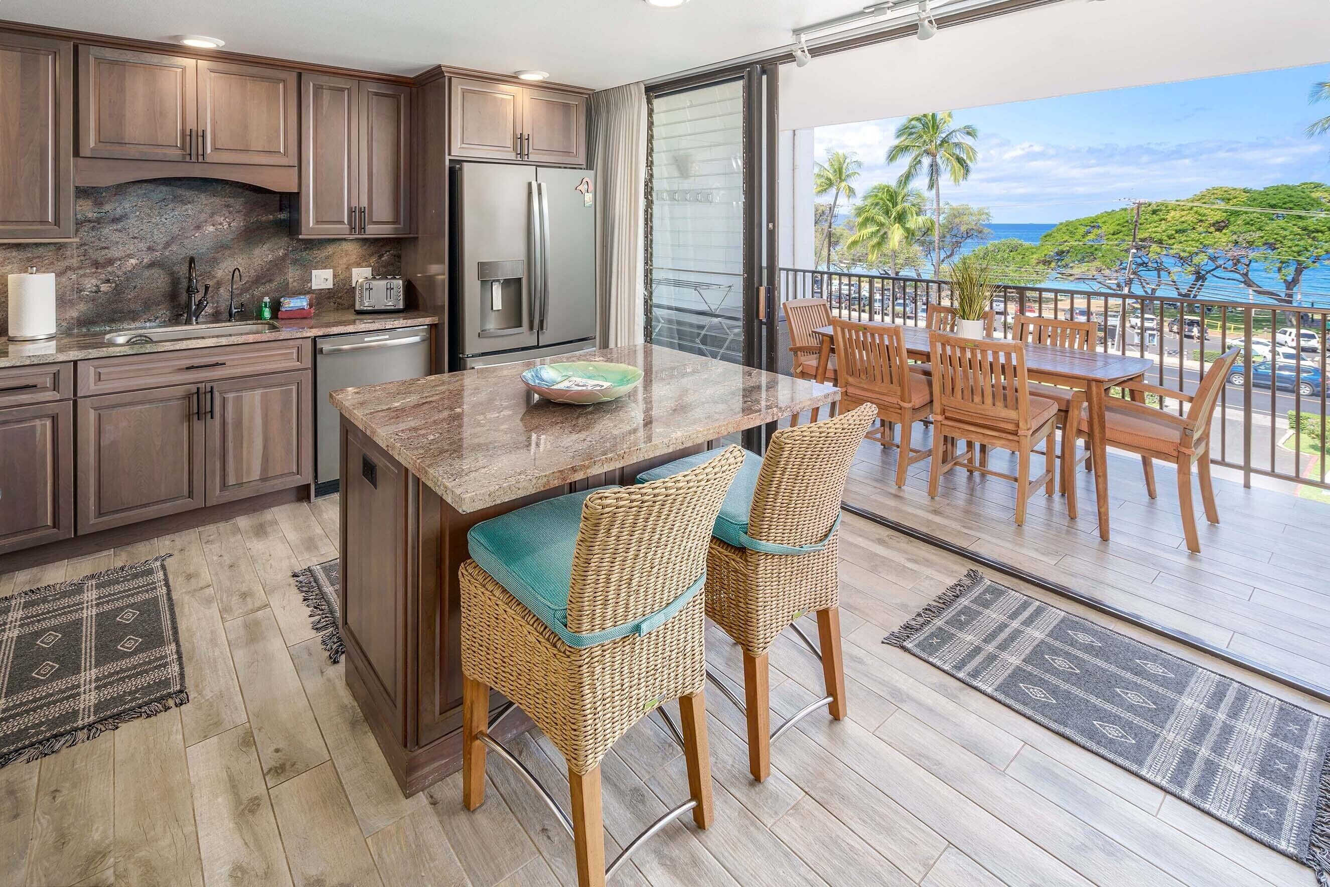 A kitchen with a large island, wooden chairs, and a view of the ocean.