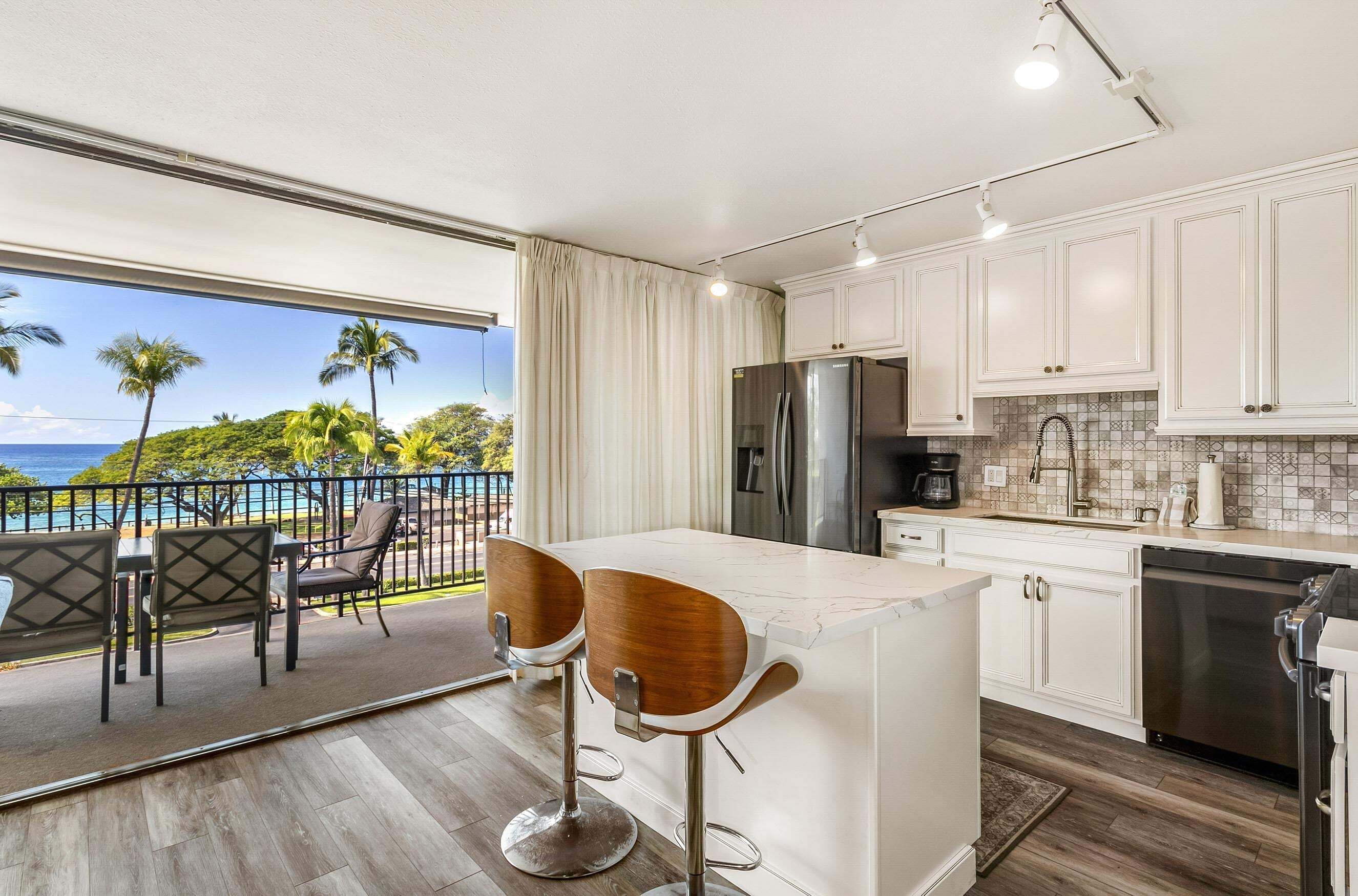 A kitchen with a large island, white cabinets, stainless steel appliances, and a view of the ocean.