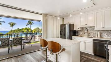 A kitchen with a large island, white cabinets, stainless steel appliances, and a view of the ocean.