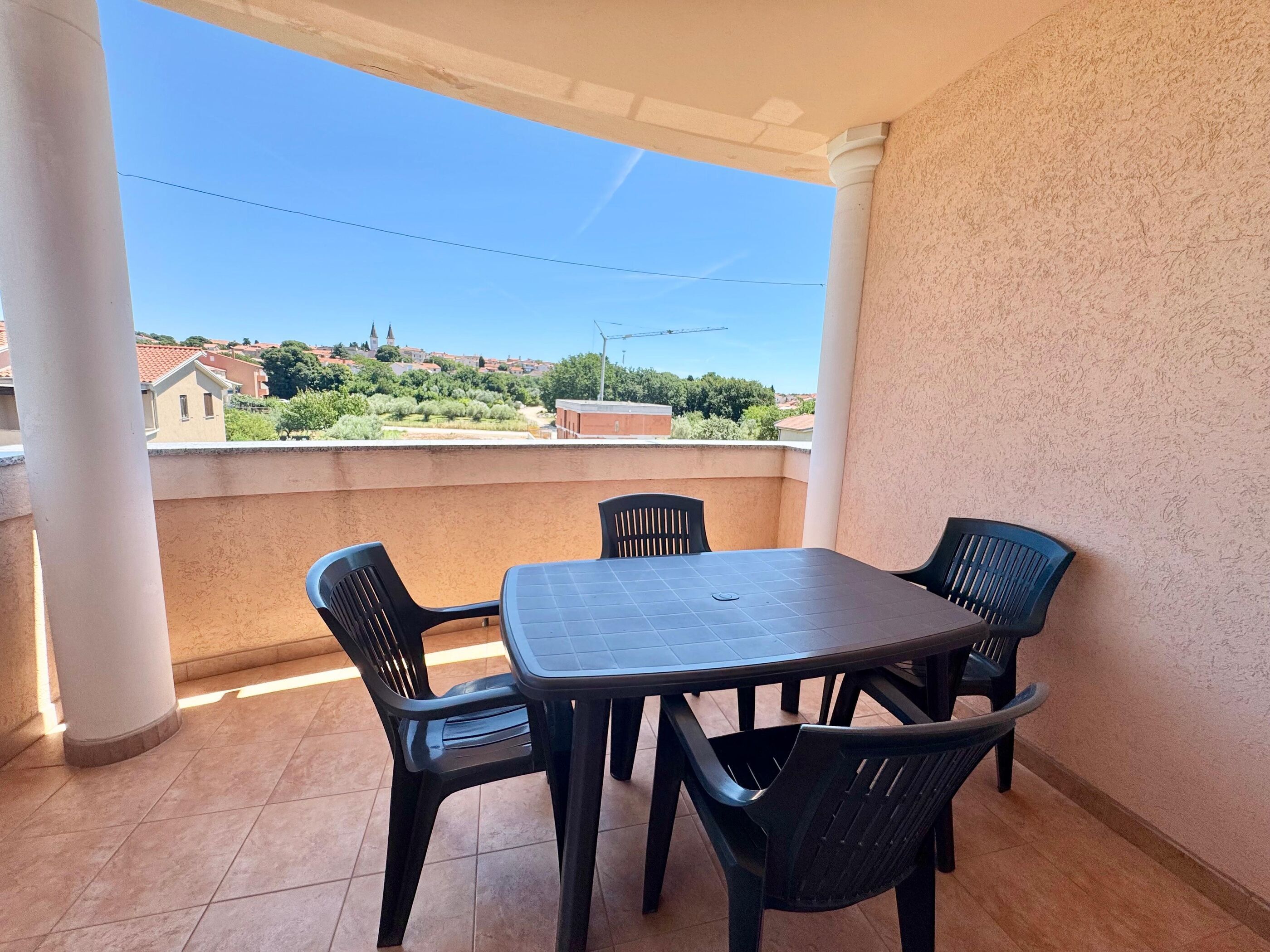 Ein Balkon mit Tisch und Stühlen, Blick auf Gebäude und einem klaren Himmel.