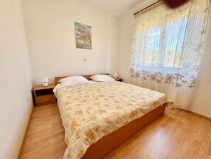 Ein Schlafzimmer mit einem Bett, Nachttischen, einer Lampe, einem Bild an der Wand und einem Fenster mit Vorhang.