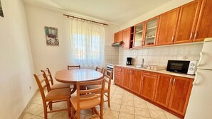 A kitchen with wooden cabinets, a round dining table, chairs, a stove, a microwave, and a refrigerator. - Apartments Cukon (16136-A7) - Medulin (Medulin)