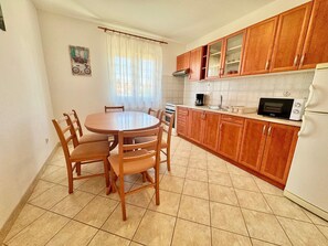 A kitchen with wooden cabinets, a round dining table, chairs, a stove, a microwave, and a refrigerator. - Apartments Cukon (16136-A7) - Medulin (Medulin)
