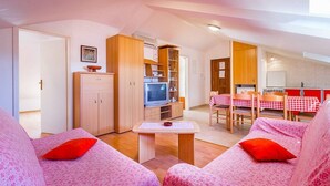 A cozy living room with a television, wooden cabinets, a dining area with a red and white checkered tablecloth, and a kitchen in the background. - Apartments Cukon (16136-A8) - Medulin (Medulin)
