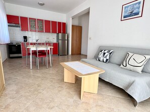 A modern kitchen with red cabinets, a dining area with a table and chairs, a grey sofa with patterned cushions, and a framed picture on the wall. - Apartments Cukon (16136-A9) - Medulin (Medulin)