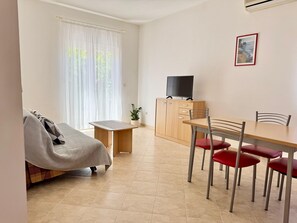 A small, well-lit room with a bed, a table with chairs, a TV on a cabinet, and a window with sheer curtains. - Apartments Cukon (16136-A9) - Medulin (Medulin)