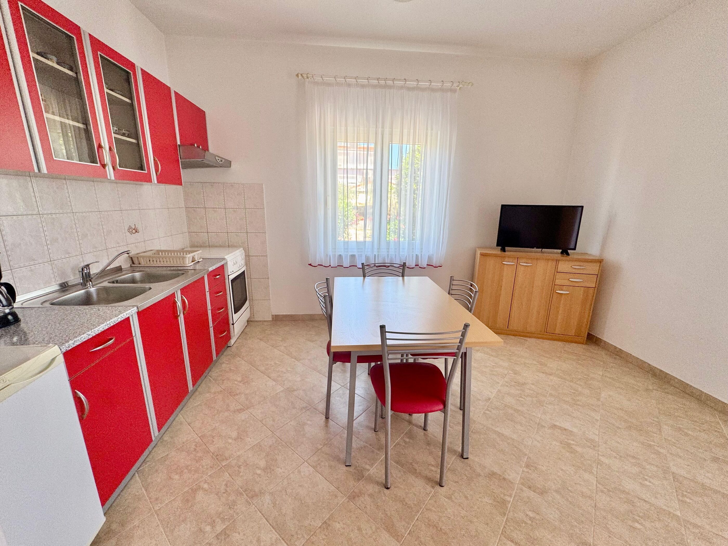 Een kleine keuken met een eettafel, stoelen, een televisie en een kast.