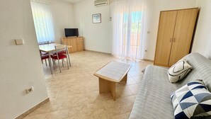 Un saló amb un sofà, una taula i una televisió. Hi ha una porta i una finestra amb cortines.