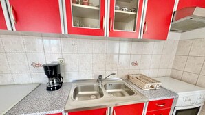 Una cuina amb armaris vermells, una doble rentavaixelles, una cafetera i una placa de cocció.