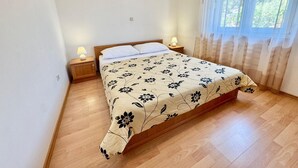 Un dormitori amb un llit de fusta, dues taules de nit amb làmpades, una finestra amb cortines i un quadre encimbellat a la paret.