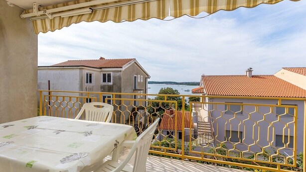 Un balcone con tavolo e sedie, ringhiera gialla e vista su edifici e sull'acqua.
