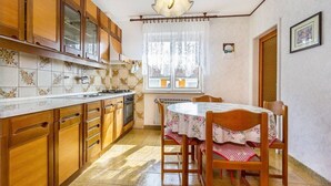 Una cucina con mobili in legno, schienale piastrellato, un tavolo da pranzo con sedie e una lampada a sospensione.