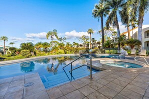 A swimming pool with a clear blue water surface, surrounded by palm trees and a building with balconies. - The Palms at Wailea (Kihei)