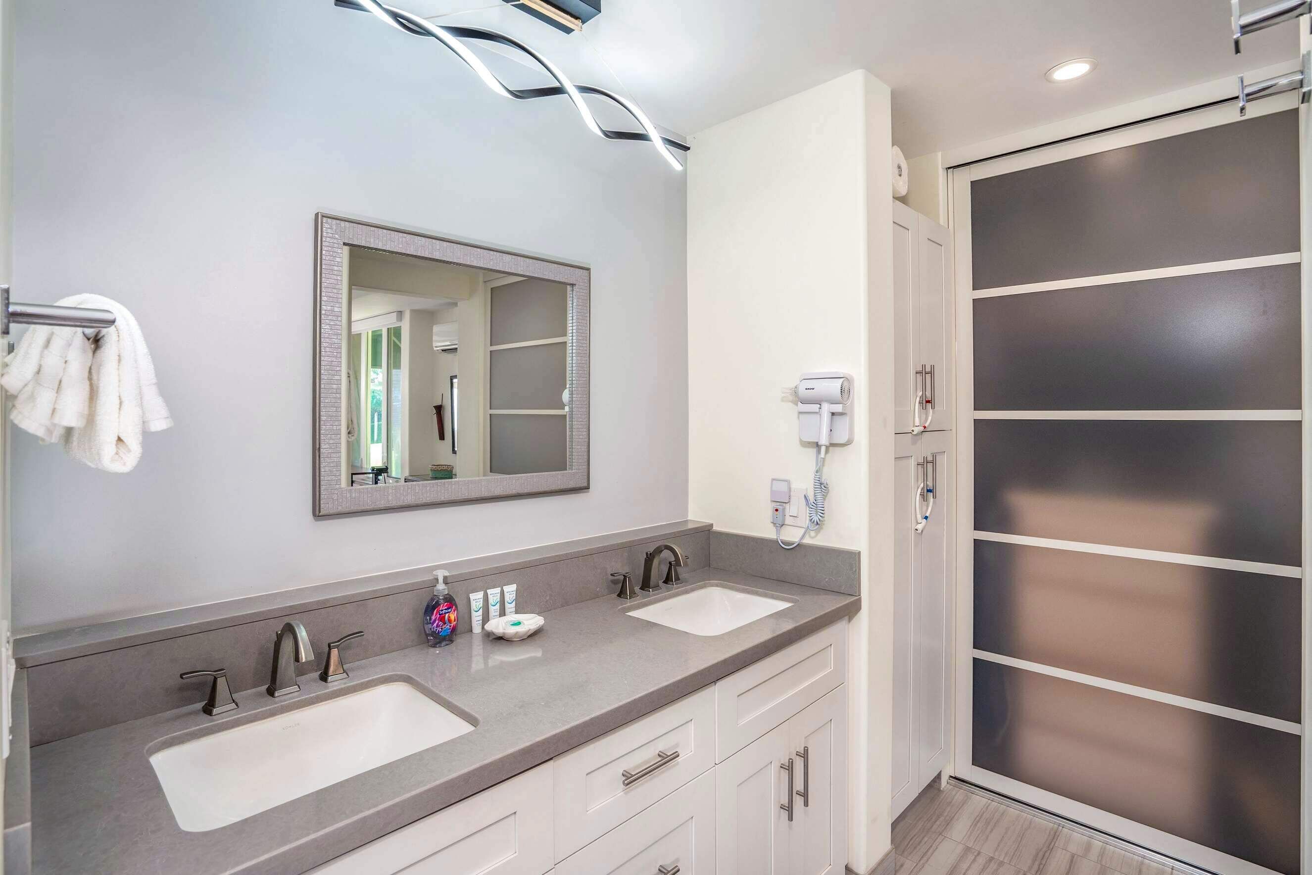 A modern bathroom with two sinks, a large mirror, and a shower enclosure.