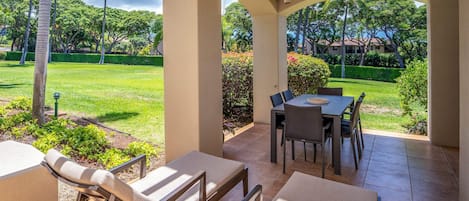 Un espacio patio al aire libre con mesa y sillas, un sillón de descanso y vista a un césped y árboles bien cuidados.