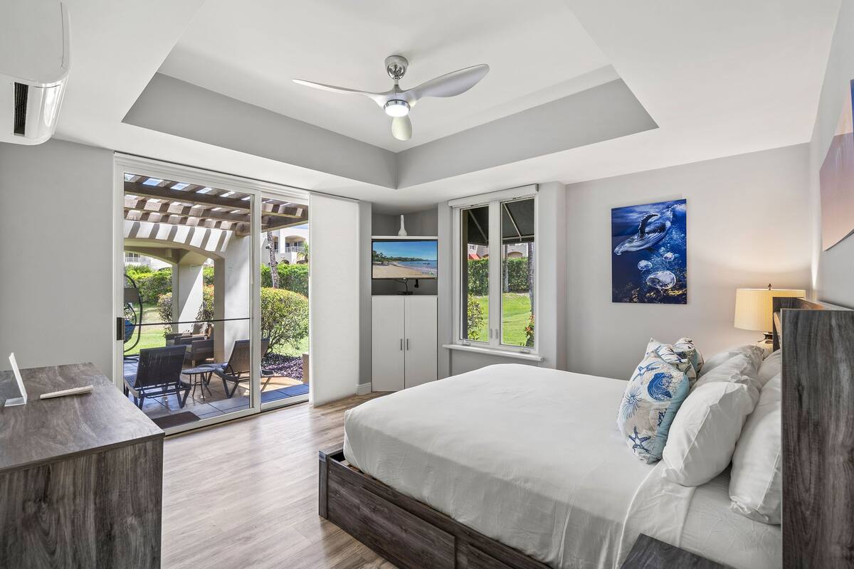A modern bedroom with a large bed, a ceiling fan, and a view of the outdoors.