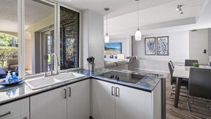 A modern kitchen with a large island, a dining area with a table and chairs, and a view of the outdoors. - The Palms at Wailea (Kihei)