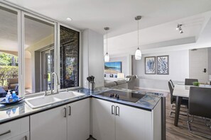 A modern kitchen with a large island, a dining area with a table and chairs, and a view of the outdoors. - The Palms at Wailea (Kihei)
