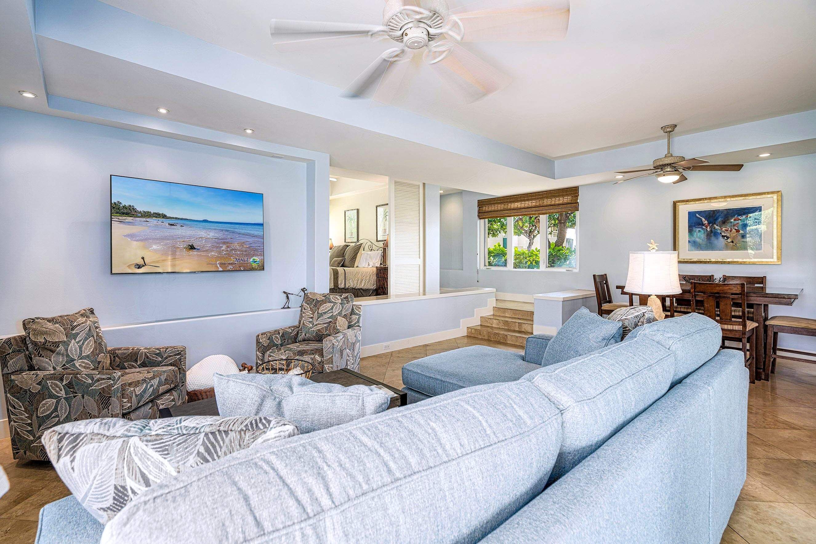 A spacious living room with a large light blue sofa, a ceiling fan, and a dining area with wooden furniture.