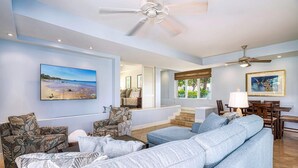 A spacious living room with a large light blue sofa, a ceiling fan, and a dining area with wooden furniture. - The Palms at Wailea (Kihei)