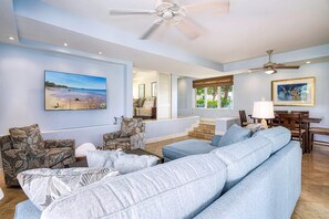 A spacious living room with a large light blue sofa, a ceiling fan, and a dining area with wooden furniture. - The Palms at Wailea (Kihei)