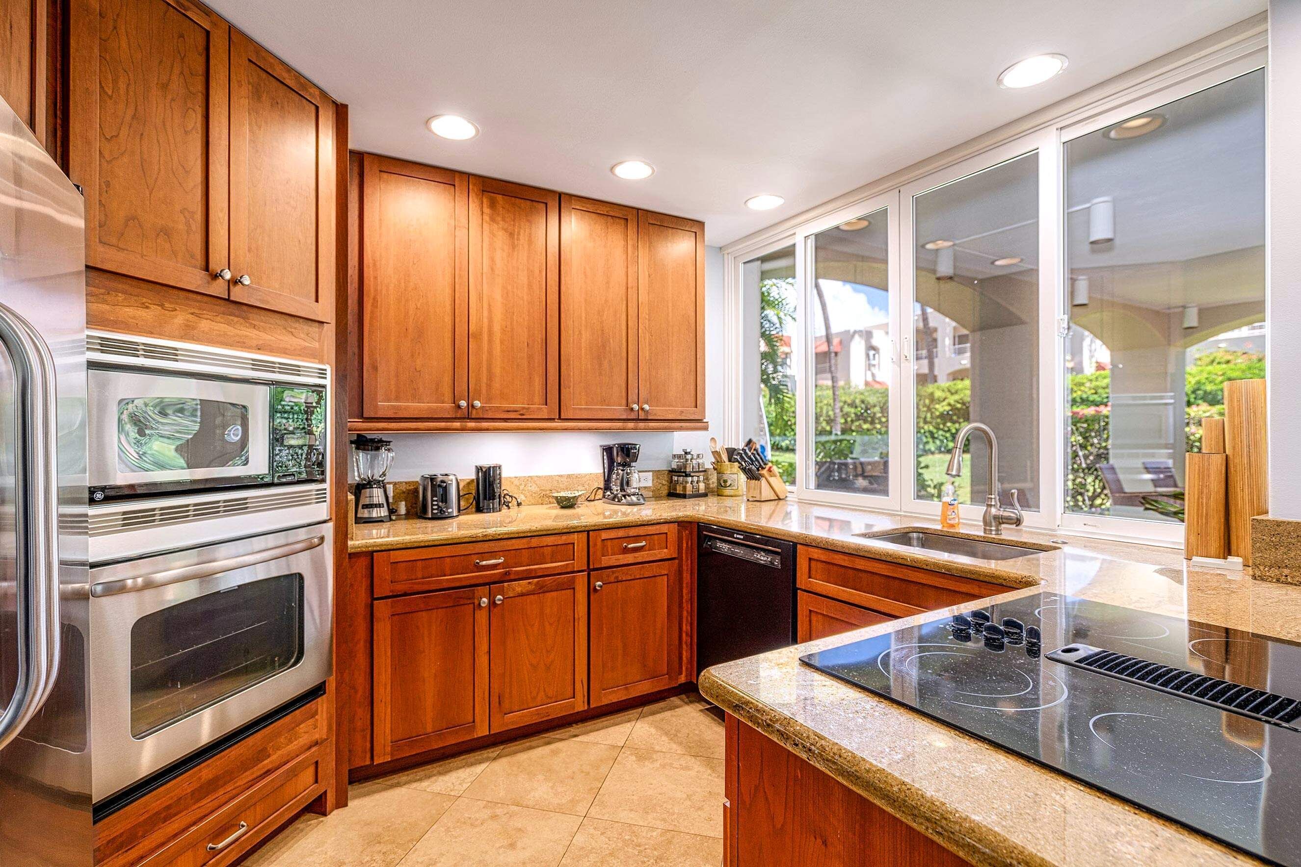 A modern kitchen with wooden cabinets, stainless steel appliances, and a large window providing a view of the outdoors.